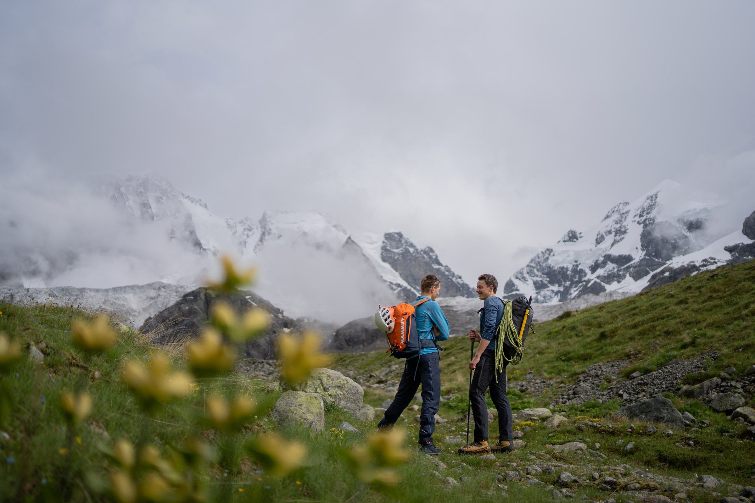 Zwei Bergsteiger auf einer Alpwiese vor verschneiten Gipfeln
