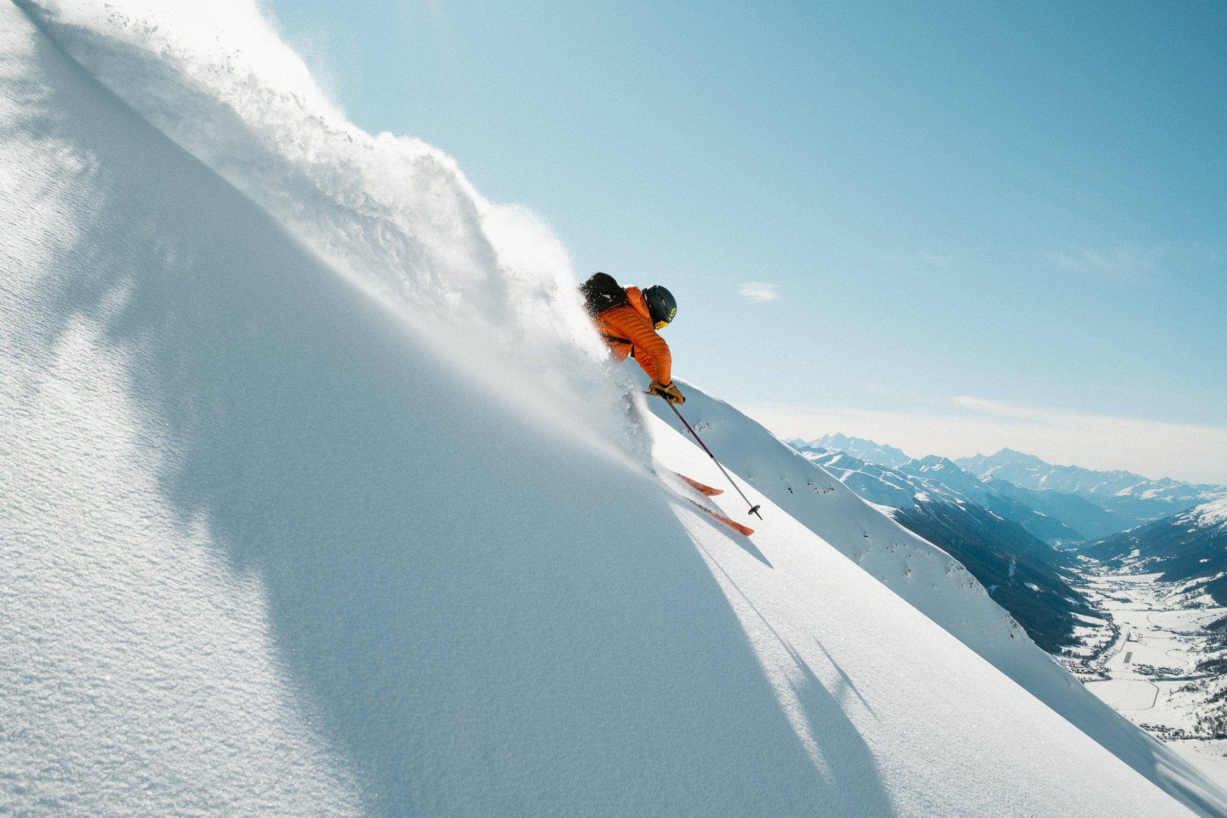 Skifahrer in orangem Anzug fährt durch tiefen Pulverschnee