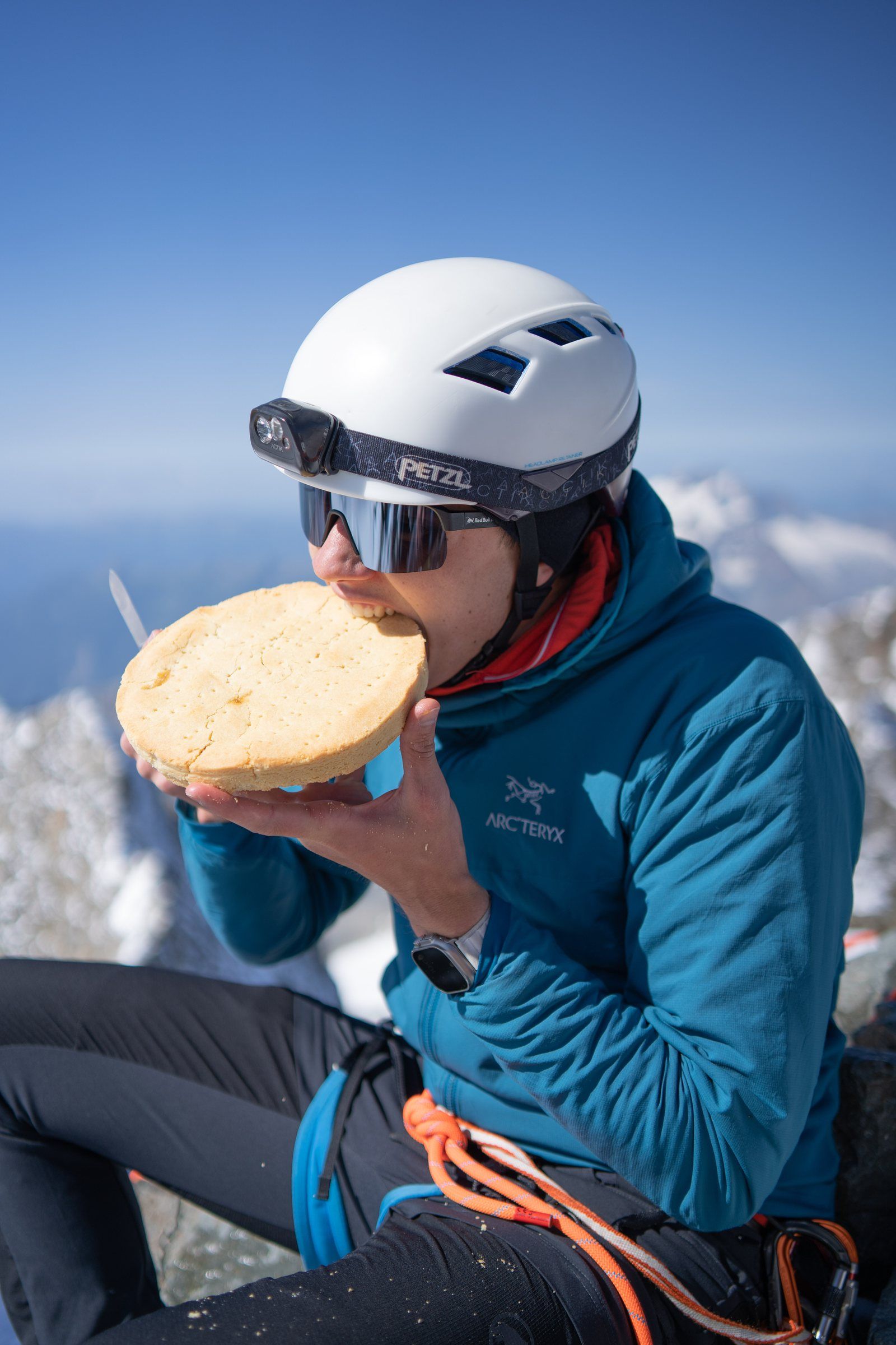 Manu mit Helm macht auf dem Gipfel Pause mit einem Brot